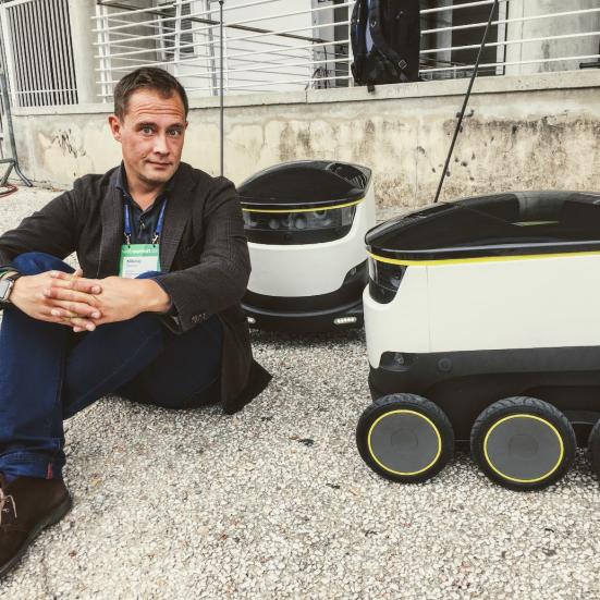 Billedet viser Nikolaj Sonne, der sidder på fortovet ved siden af to robotter.
