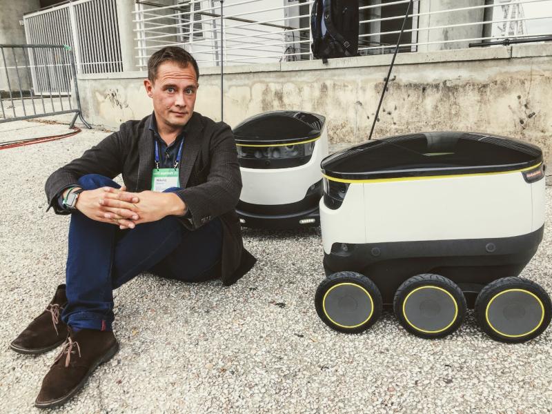 Billedet viser Nikolaj Sonne, der sidder på fortovet ved siden af to robotter.